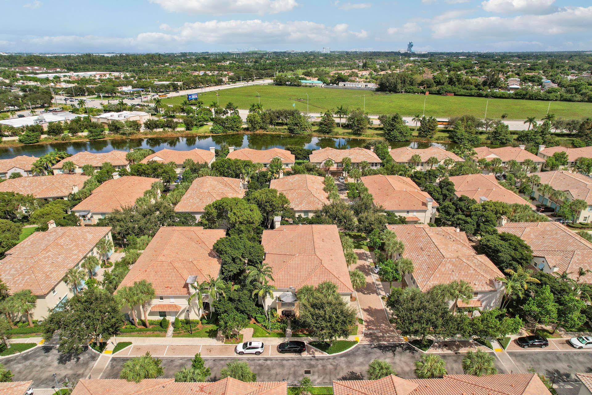 4326 Cascada Circle, Hollywood, FL 33024 Aerial perspective of a multi-unit residential community featuring terracotta-style roof tiles, paved thoroughfares, interspersed mature landscaping, and a central water feature