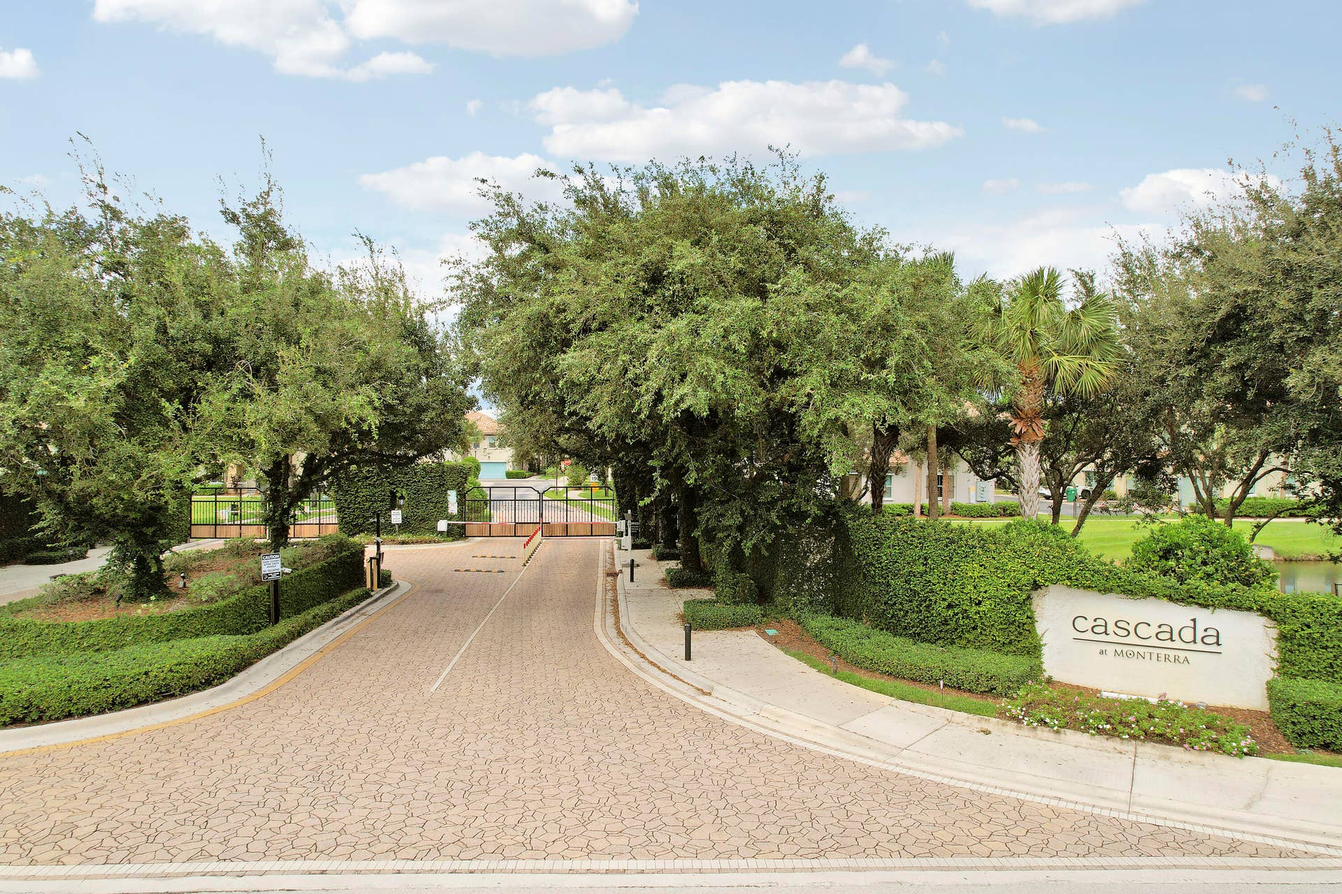 4326 Cascada Circle, Hollywood, FL 33024 Gated entrance featuring decorative paver driveway, manicured landscaping, and mature trees