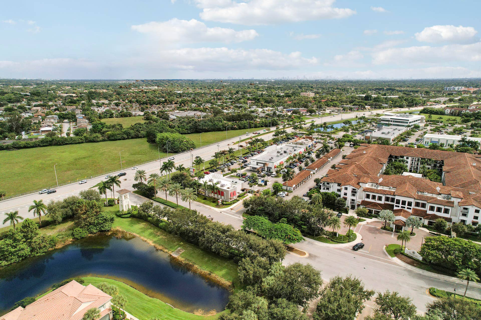 4326 Cascada Circle, Hollywood, FL 33024 Aerial perspective featuring a multi-story building with a clay tile roof, a central courtyard, and a prominent water feature surrounded by established palm trees and manicured landscaping