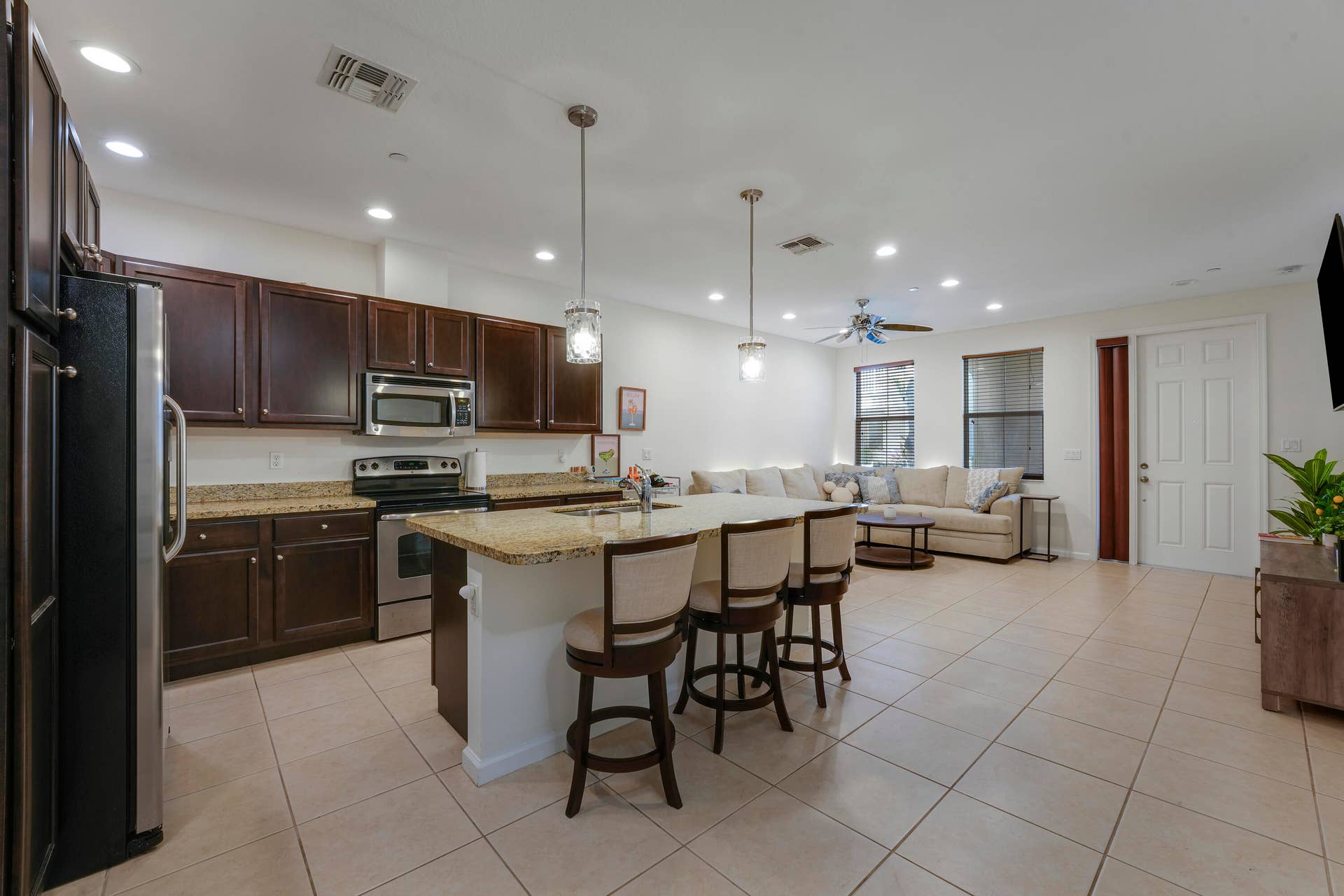 4326 Cascada Circle, Hollywood, FL 33024 Open-concept kitchen featuring dark wood cabinetry, stone countertops, a central island with bar seating, stainless steel appliances, and tile flooring