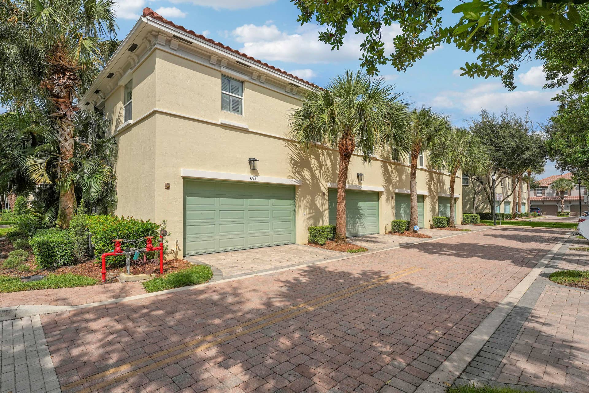 4326 Cascada Circle, Hollywood, FL 33024 Stucco exterior featuring multiple garage bays, a terracotta-style tile roof, and brick paver driveway, surrounded by mature palm trees