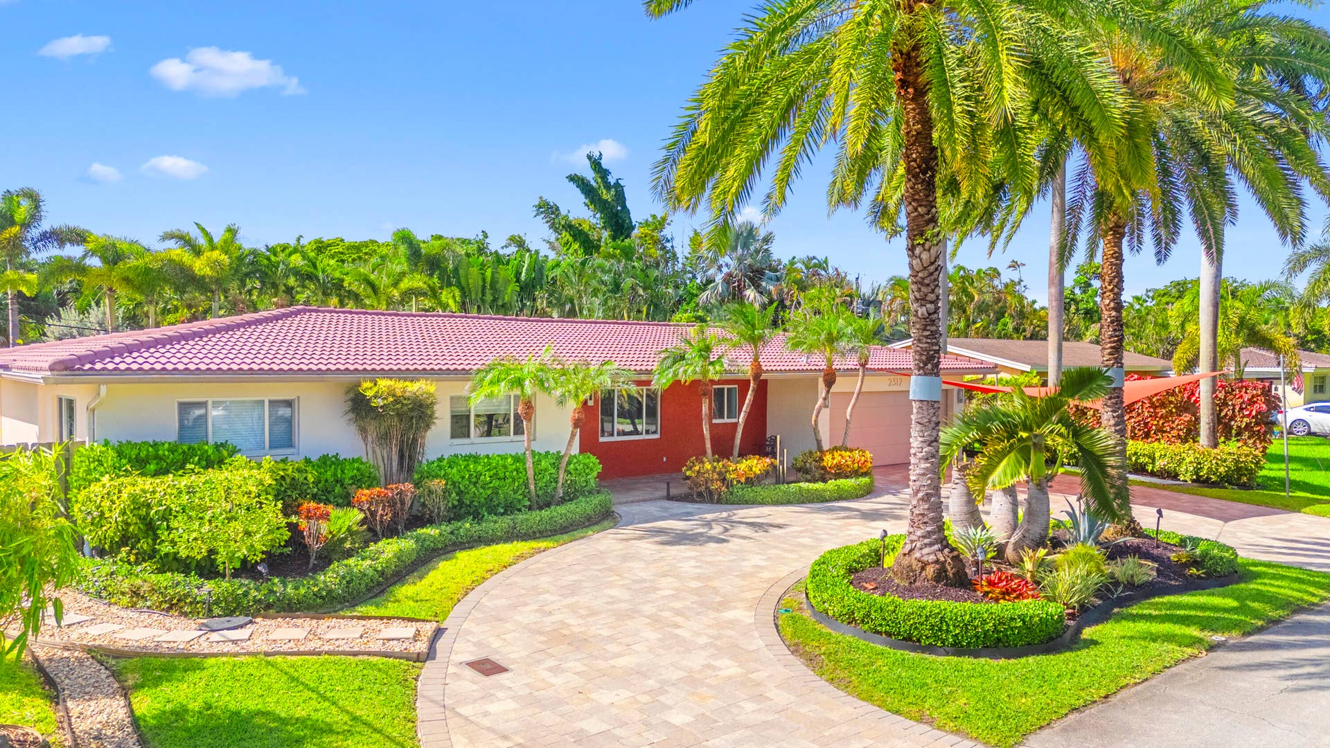 2317 NW 6th Avenue, Wilton Manors, FL 33311 Single-story residence featuring a tile roof, paved circular driveway, manicured landscaping, and mature palm trees