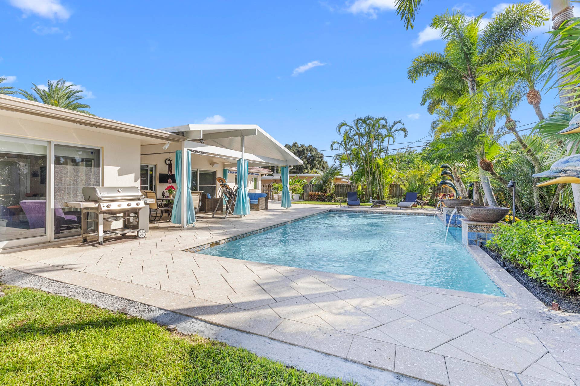 2317 NW 6th Avenue, Wilton Manors, FL 33311 Outdoor living space featuring a covered patio, swimming pool with water features, patterned paver decking, and mature palm trees