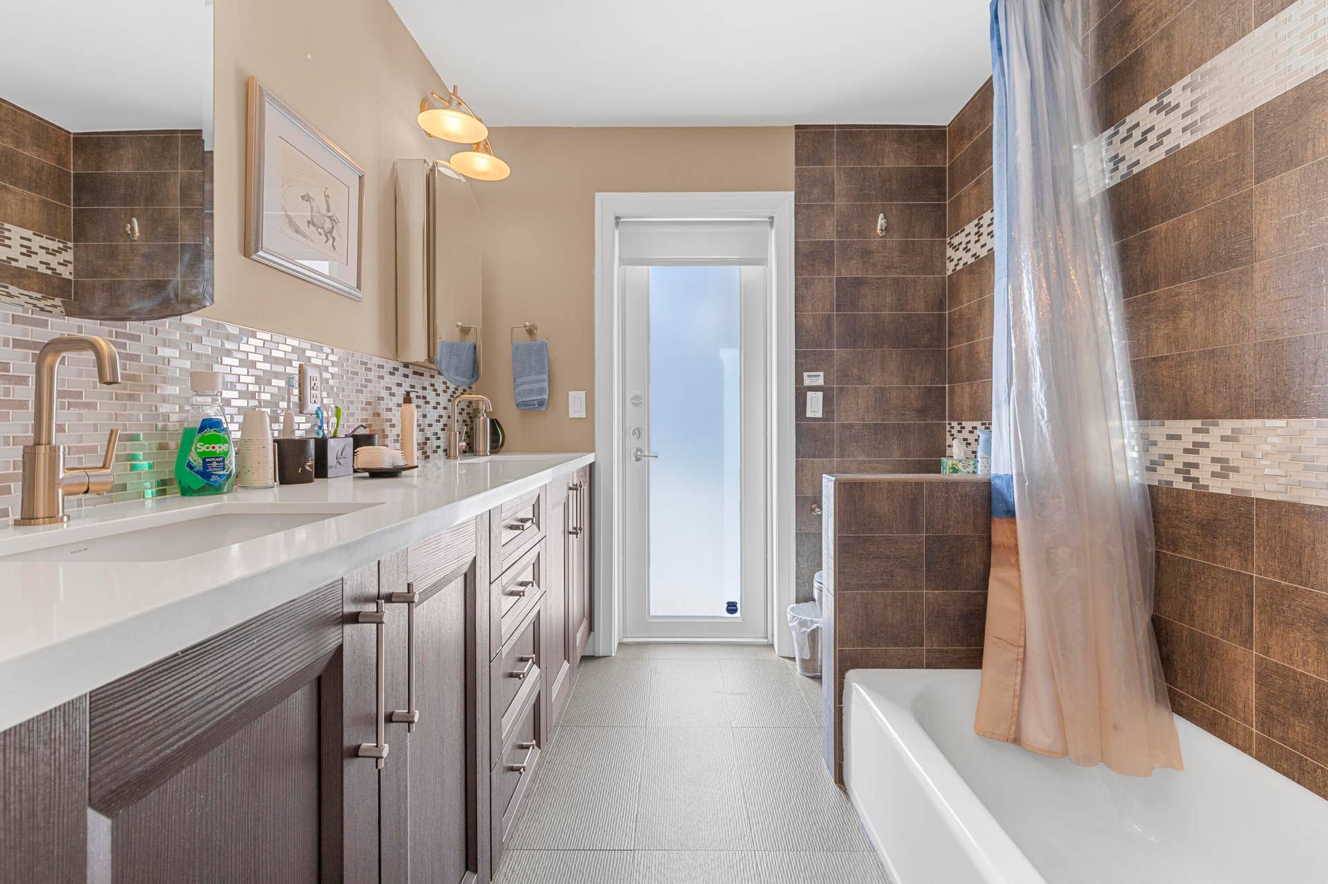 2317 NW 6th Avenue, Wilton Manors, FL 33311 Bathroom featuring custom wood-finish cabinetry, white solid-surface countertop, metallic finish fixtures, glass tile backsplash, and a tiled shower surround