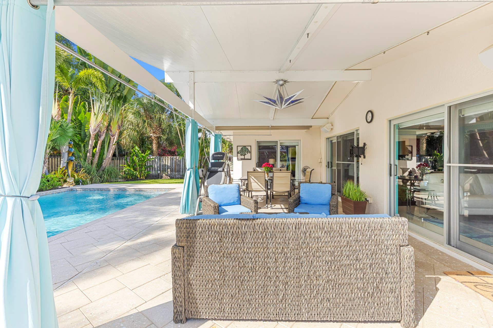 2317 NW 6th Avenue, Wilton Manors, FL 33311 Covered patio featuring a paved stone deck, ceiling-mounted lighting fixture, and sliding glass door access, complemented by an inground swimming pool and privacy fencing