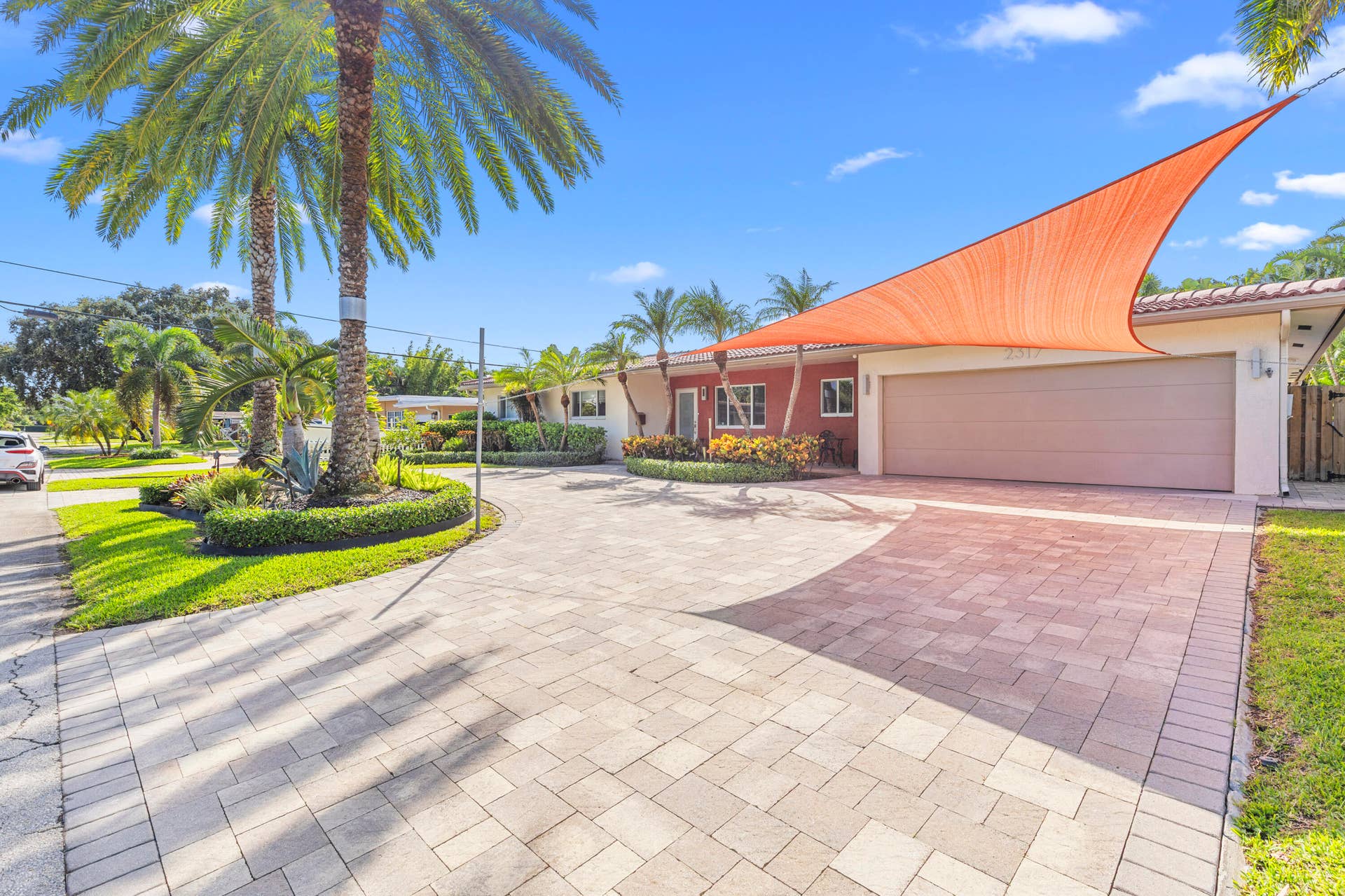 2317 NW 6th Avenue, Wilton Manors, FL 33311 Exterior facade featuring a two-car garage, paver driveway, tiled roof, mature palm trees, and manicured landscaping