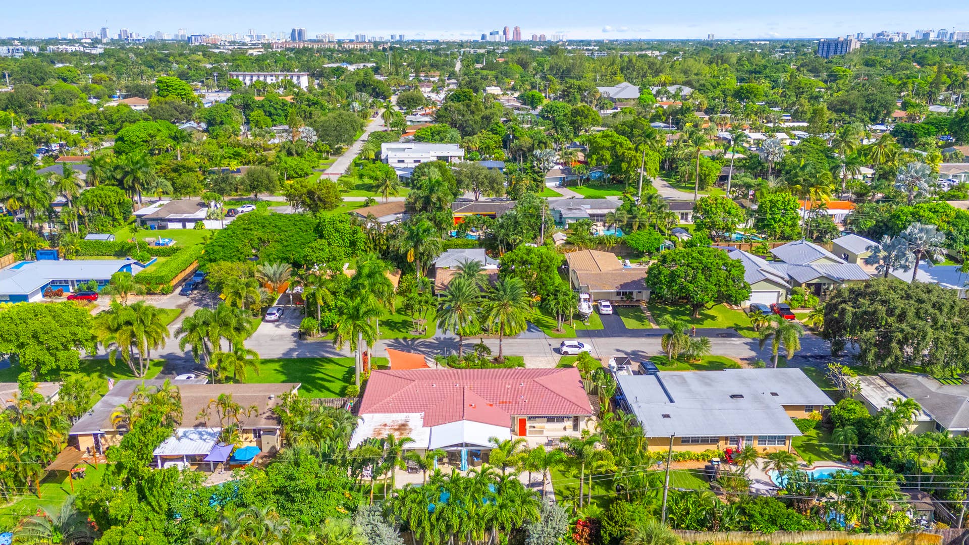 2317 NW 6th Avenue, Wilton Manors, FL 33311 Aerial perspective of a property featuring a red metal roof, expansive lawn, mature landscaping, and a fenced backyard