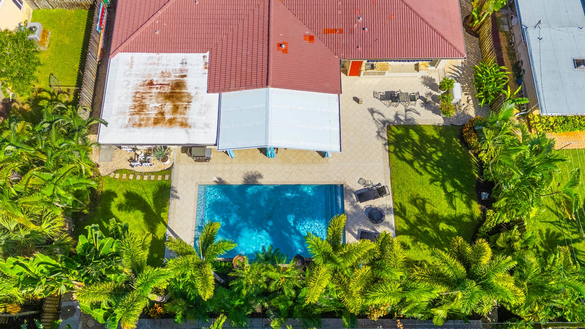 2317 NW 6th Avenue, Wilton Manors, FL 33311 Aerial view of the backyard featuring a rectangular swimming pool, expansive paved patio, covered porch, and mature perimeter landscaping