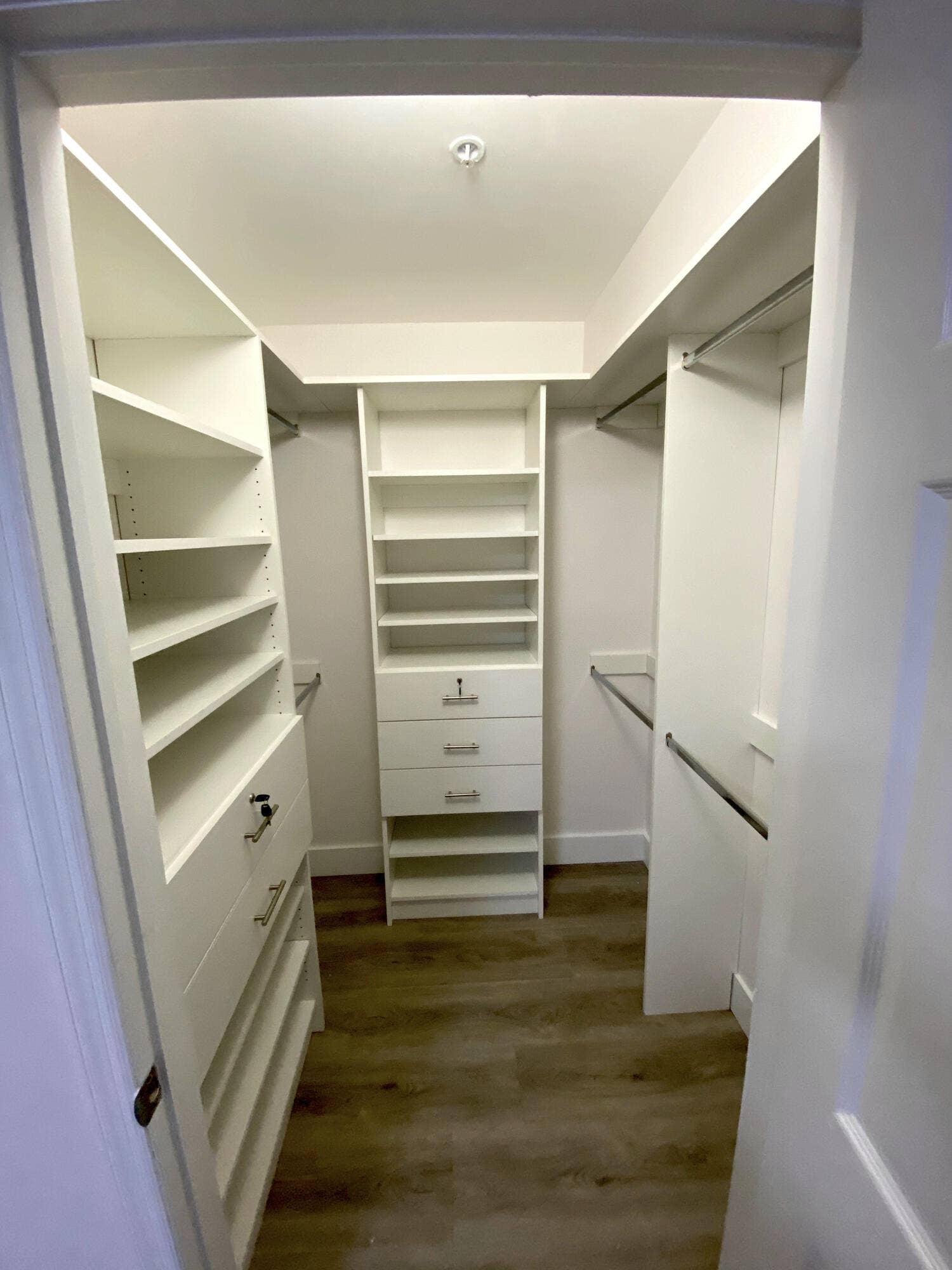 2941 NE 185TH Street, #1303, Aventura, FL 33180 Walk-in closet featuring white custom built-in shelving, multi-drawer storage units with integrated locks, wood-finish flooring, and dual-level metal hanging rods