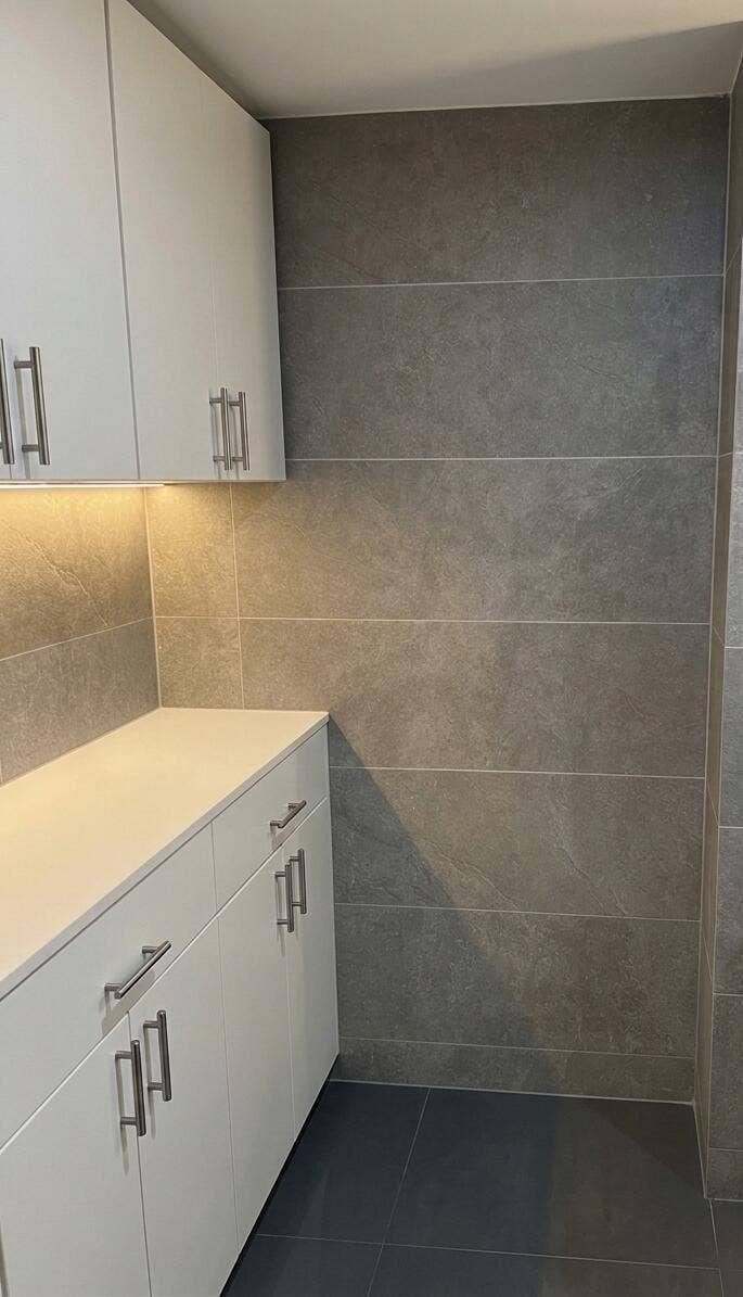 2941 NE 185TH Street, #1303, Aventura, FL 33180 Built-in white cabinetry featuring metallic hardware, solid-surface countertop, integrated under-cabinet lighting, and large-format grey tile wall cladding