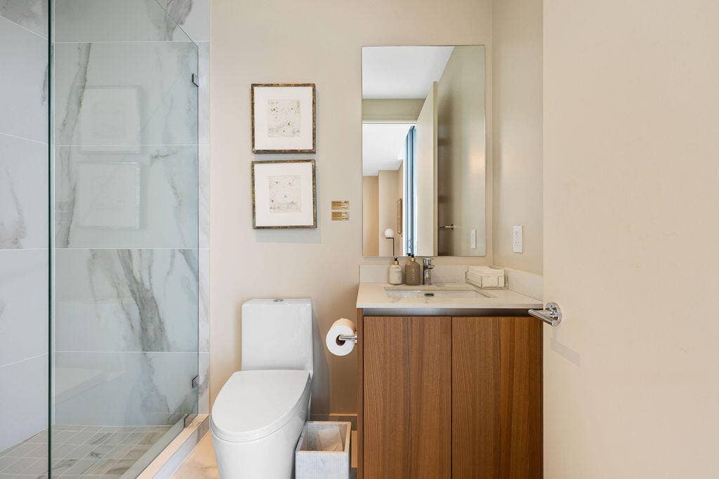 Bathroom featuring a glass-enclosed shower with large-format tile surround, a wood-finish vanity with a stone-surface countertop, an integrated sink, and a wall-mounted mirror