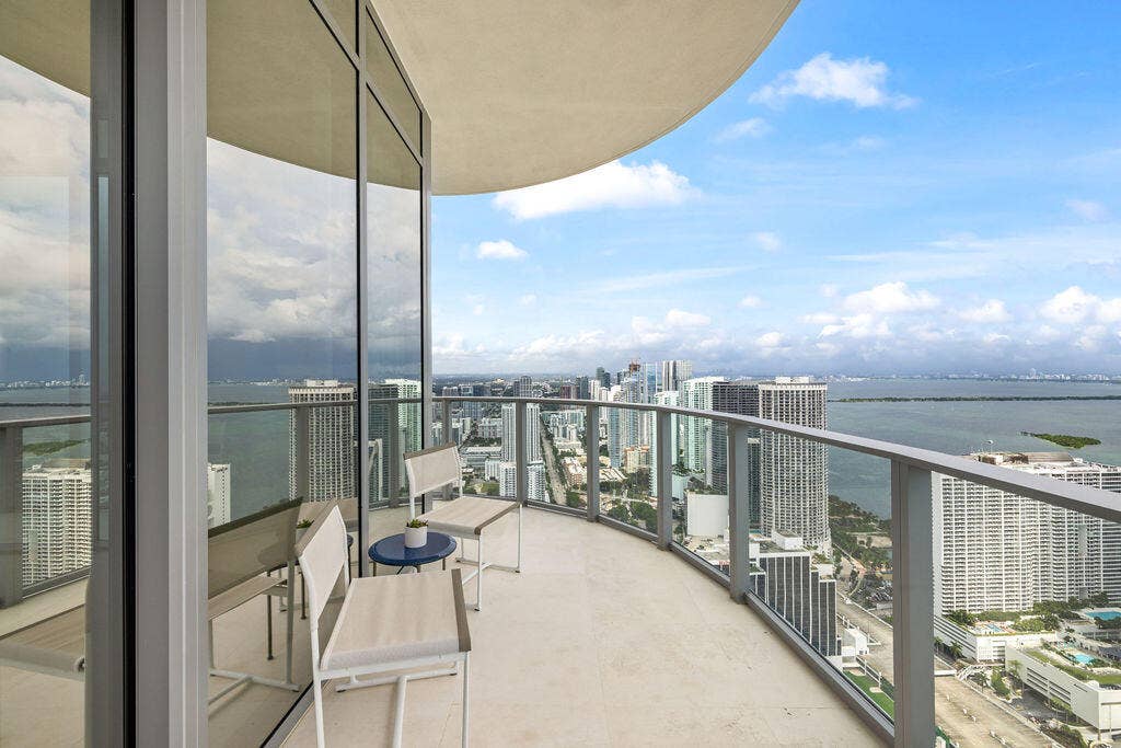 Curved private balcony featuring floor-to-ceiling glass wall, light-toned stone tile flooring, and a metal railing