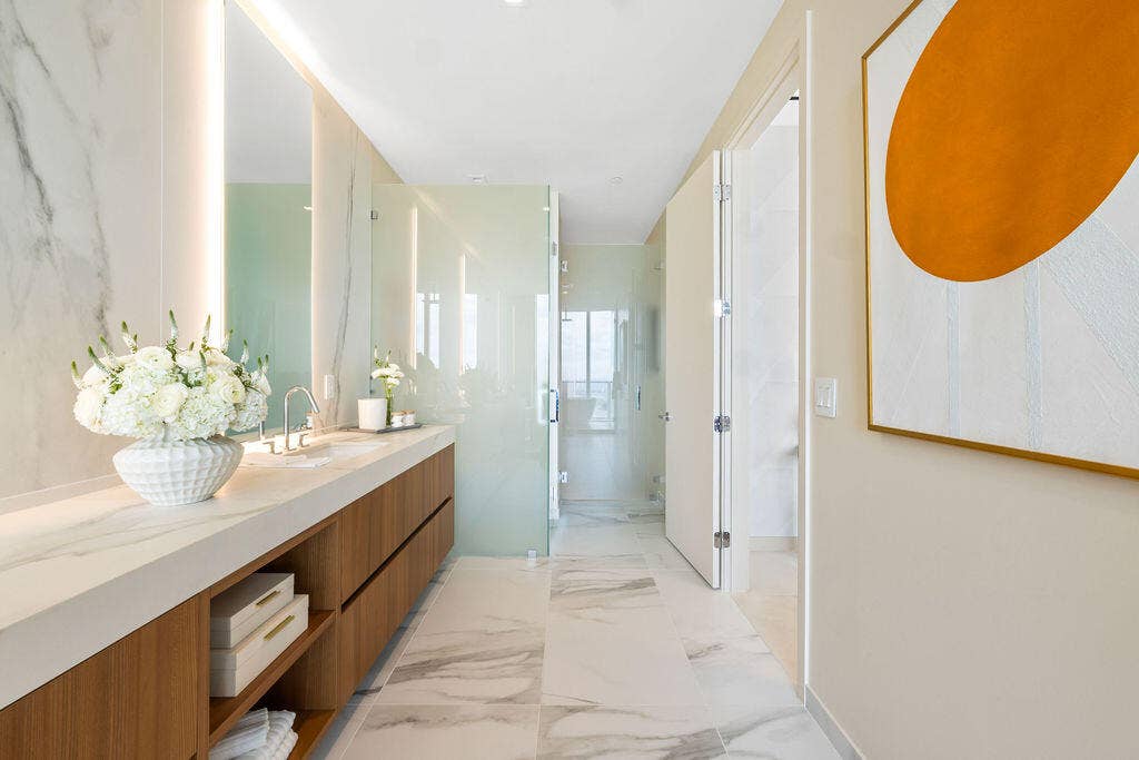 Floating wood-finish vanity with countertop, integrated wall-to-ceiling mirror, stone-finish tile flooring, and glass-enclosed shower