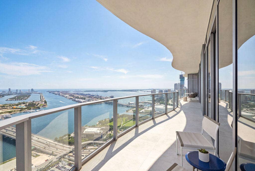 Curved balcony featuring a glass railing system, concrete flooring, and an overhanging structural soffit