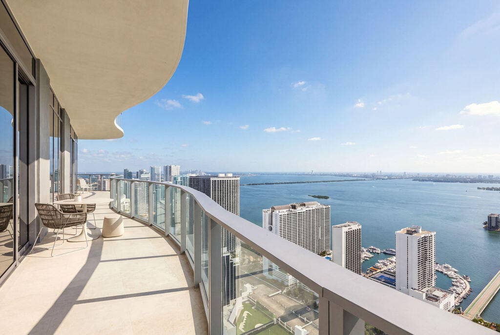 Curved balcony with concrete flooring, glass panel railings, and a cantilevered roof covering