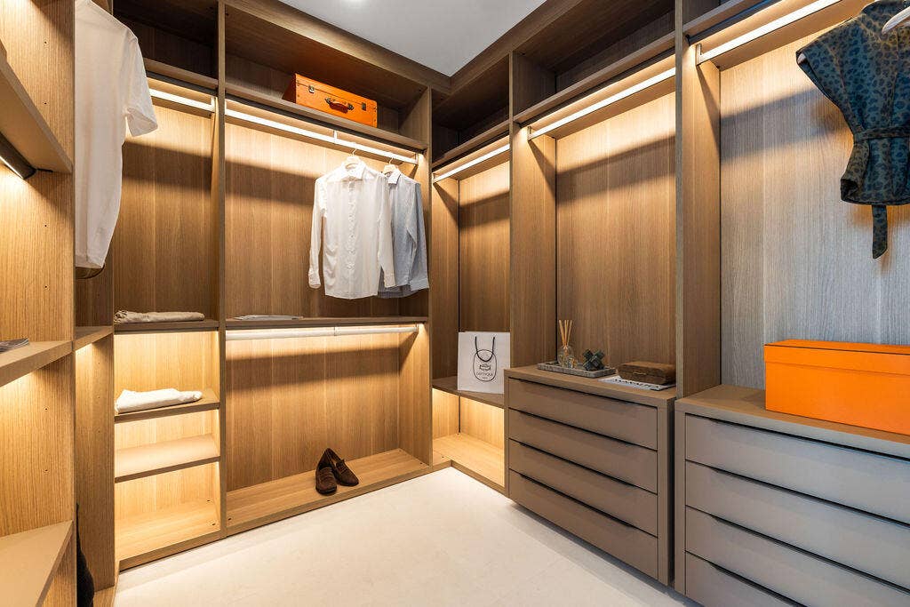 Custom walk-in closet featuring built-in wood-finish shelving, integrated LED accent lighting, hanging rods, and multi-drawer storage cabinetry