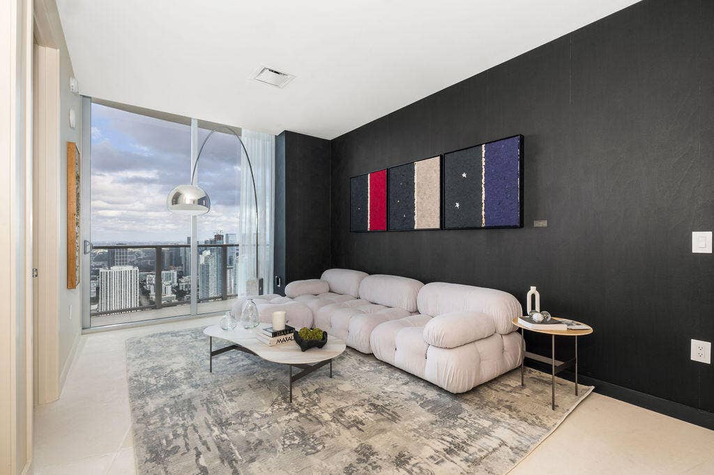 Floor-to-ceiling glass paneling featuring a metal frame and sliding glass door, providing a panoramic outlook, complemented by neutral tile flooring and a distinctive matte black accent wall