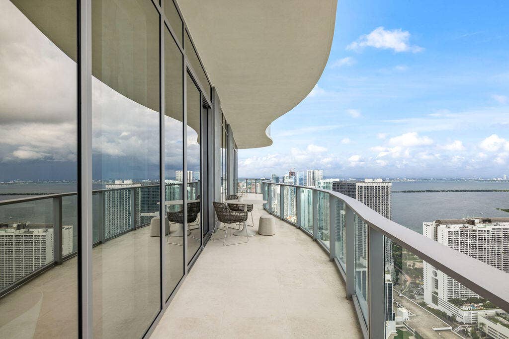 Expansive curved balcony featuring floor-to-ceiling glass paneling, metal railings, and stone-finish flooring