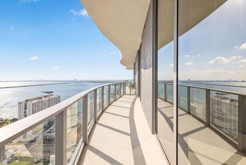 Curved exterior terrace featuring floor-to-ceiling glass panel walls, a metal railing system, and stone-finish flooring