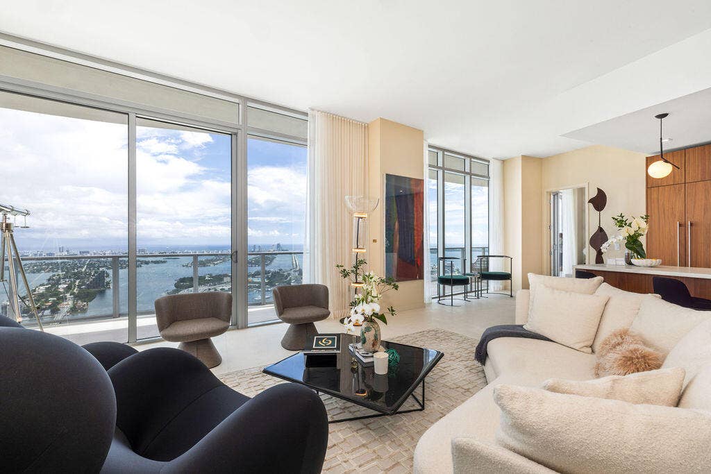 Floor-to-ceiling glass windows, expansive private balcony with glass railing, open-concept living area, custom flat-panel wood cabinetry, and neutral tile flooring
