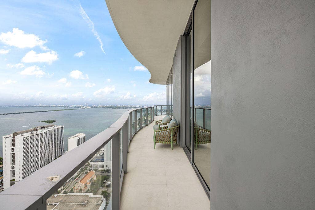 Curved wrap-around balcony featuring a glass panel railing, tile flooring, and floor-to-ceiling glass wall