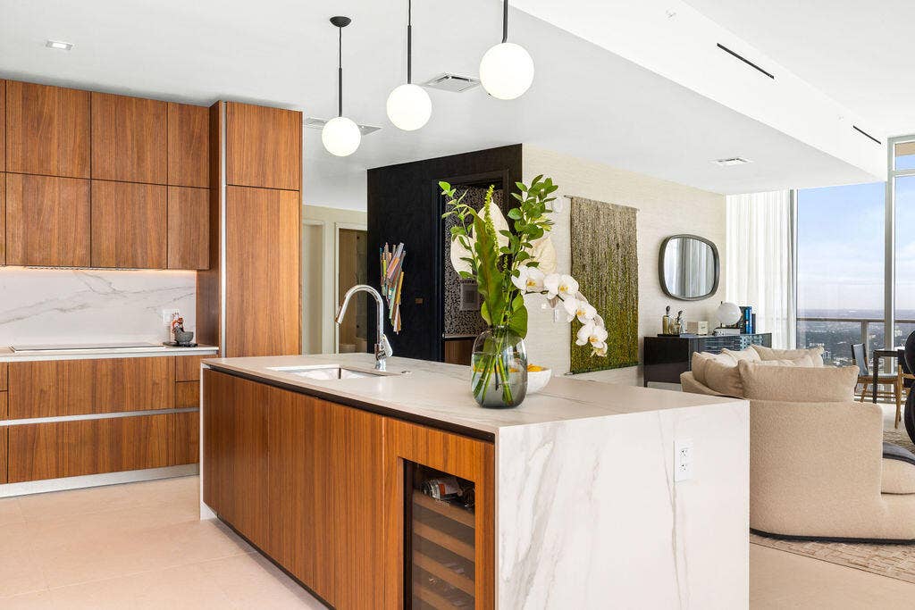 Kitchen featuring wood-finish cabinetry, waterfall-edge stone countertops, a built-in wine refrigerator, and suspended globe pendant lighting