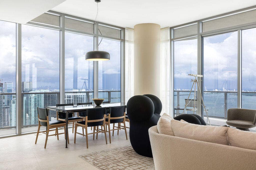 Floor-to-ceiling glass walls, wrap-around balcony with glass railing, large-format tile flooring, cylindrical structural column, and modern matte black pendant lighting