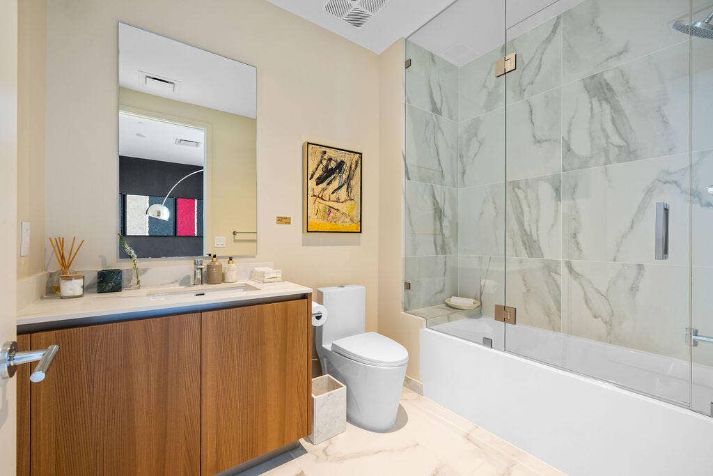 Bathroom featuring a wood-finish vanity with a light-toned countertop, a frameless glass shower enclosure, large-format tile shower surround, and tile flooring
