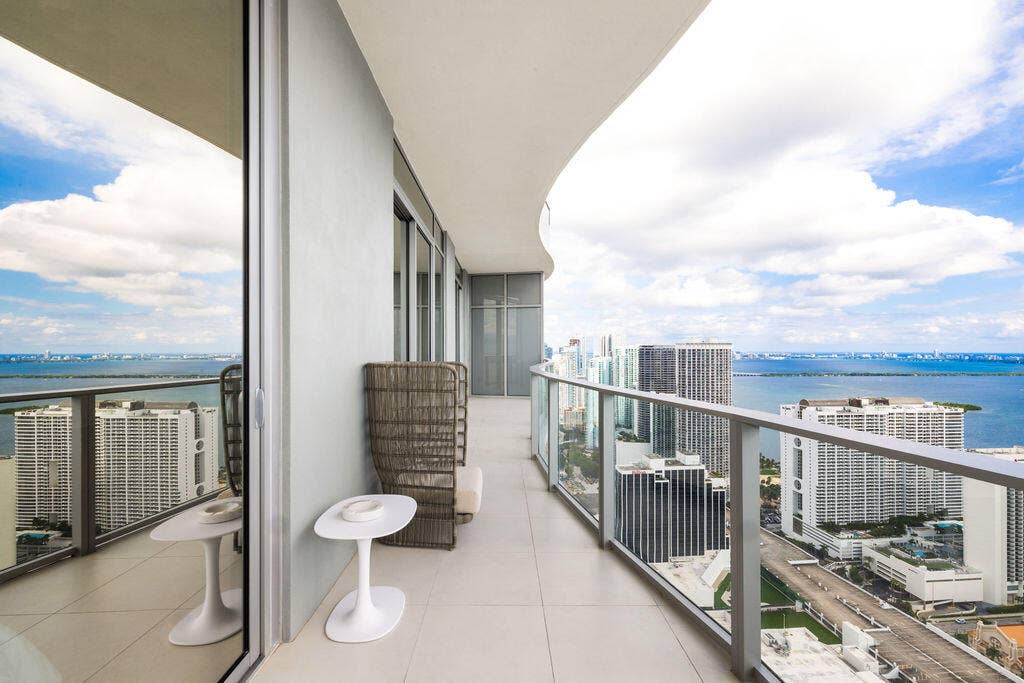 Expansive wrap-around balcony featuring large-format tile flooring, a curved architectural design, and floor-to-ceiling glass paneling with metal railing