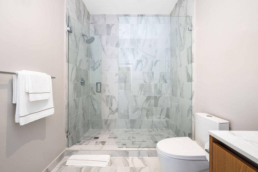 Walk-in shower featuring a frameless glass enclosure, floor-to-ceiling stone-finish wall tiles, and a wall-mounted shower head