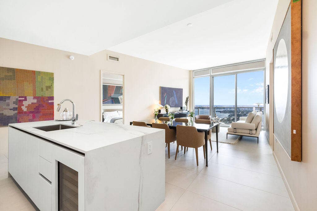 Center island featuring a white stone countertop, undermount sink, and integrated wine refrigeration, complemented by large-format tile flooring and floor-to-ceiling windows