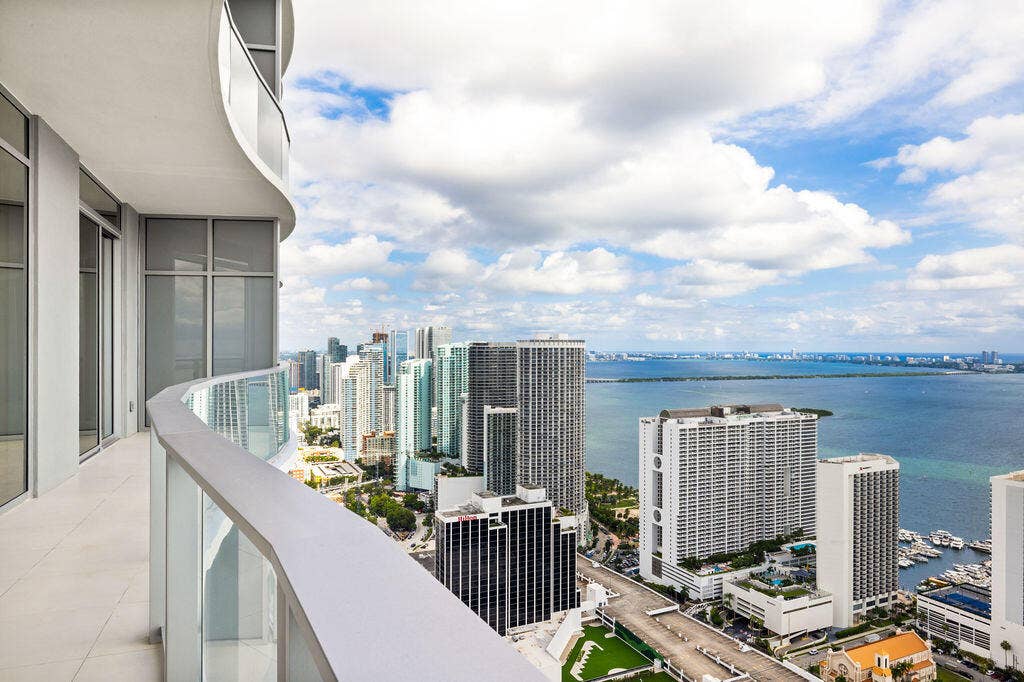Curved exterior balcony with glass railing, large-format tile flooring, and expansive floor-to-ceiling windows