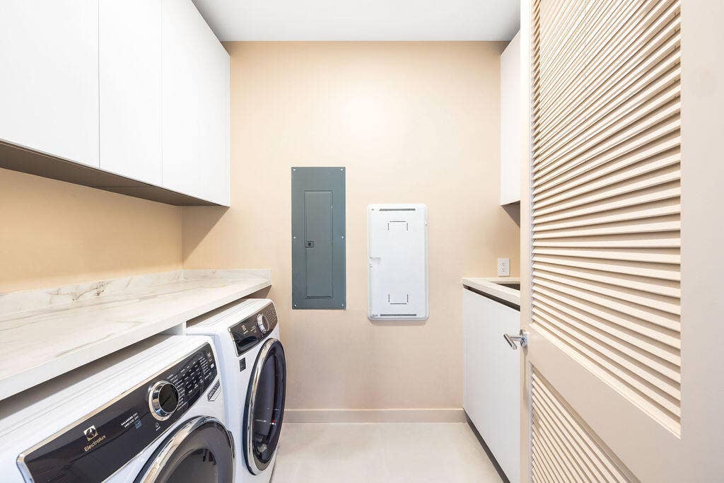 Laundry room featuring white shaker-style wall cabinetry, stone-finish countertops, and a louvered door