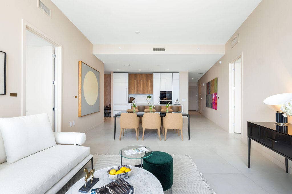 Open-concept interior featuring light-toned flooring, high ceilings, custom wood and white cabinetry, a built-in oven, and a kitchen island with stone countertop
