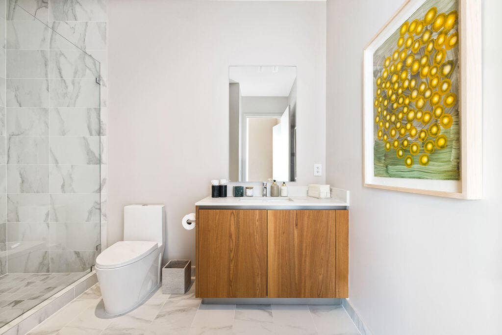Bathroom featuring a wood-finish vanity with a stone countertop, a glass-enclosed shower with large-format tile surround, a wall-mounted mirror, and tile flooring