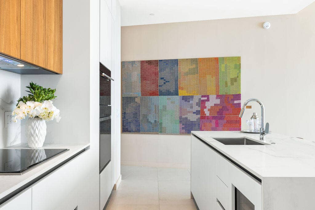 Kitchen featuring minimalist white cabinetry, wood-finish upper cabinets, integrated wall oven, white stone-surface countertops, and a stainless steel undermount sink with a gooseneck faucet