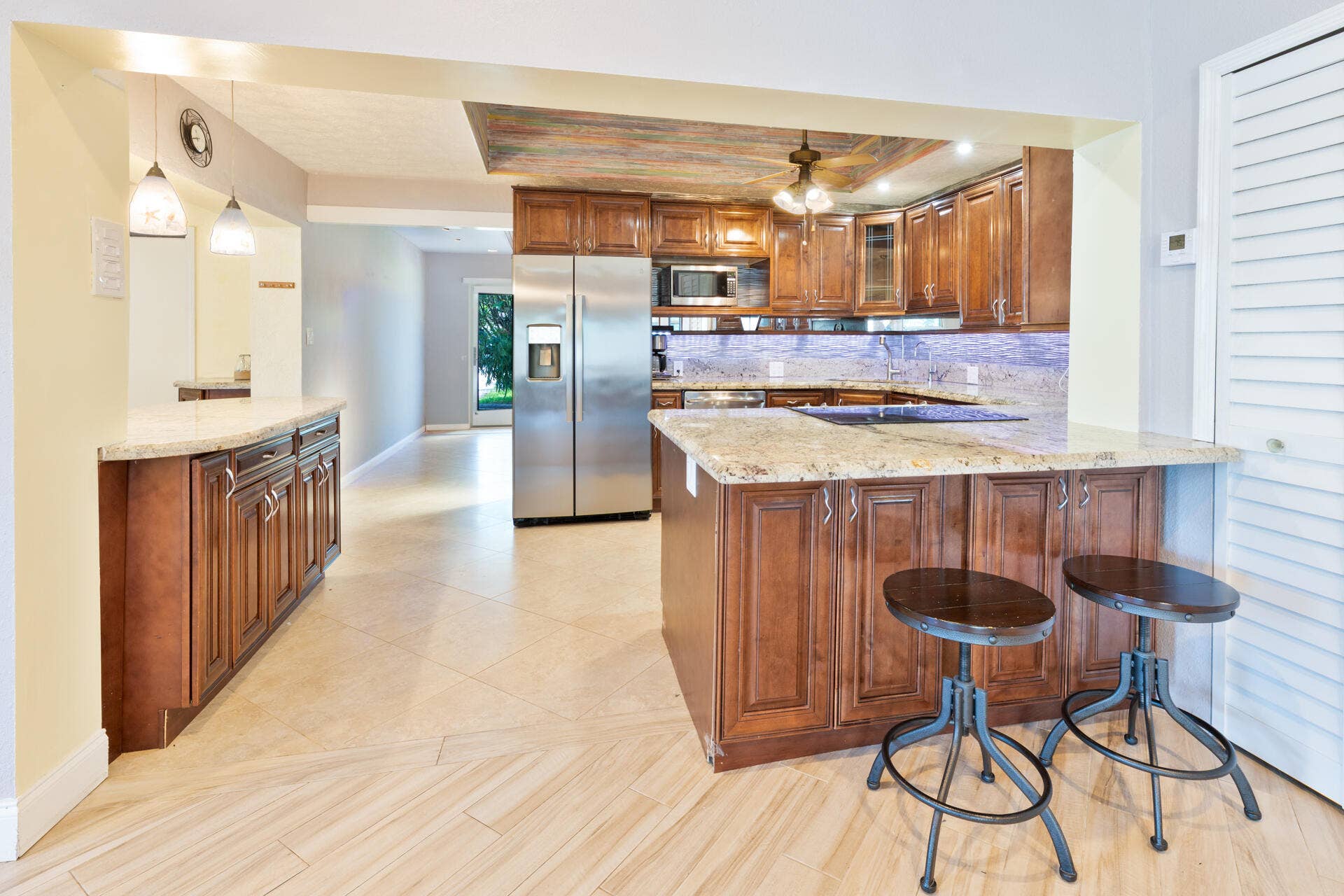 Kitchen featuring raised-panel wood cabinetry, stone countertops, stainless steel appliances, a recessed ceiling detail, and diagonal-patterned floor tiling