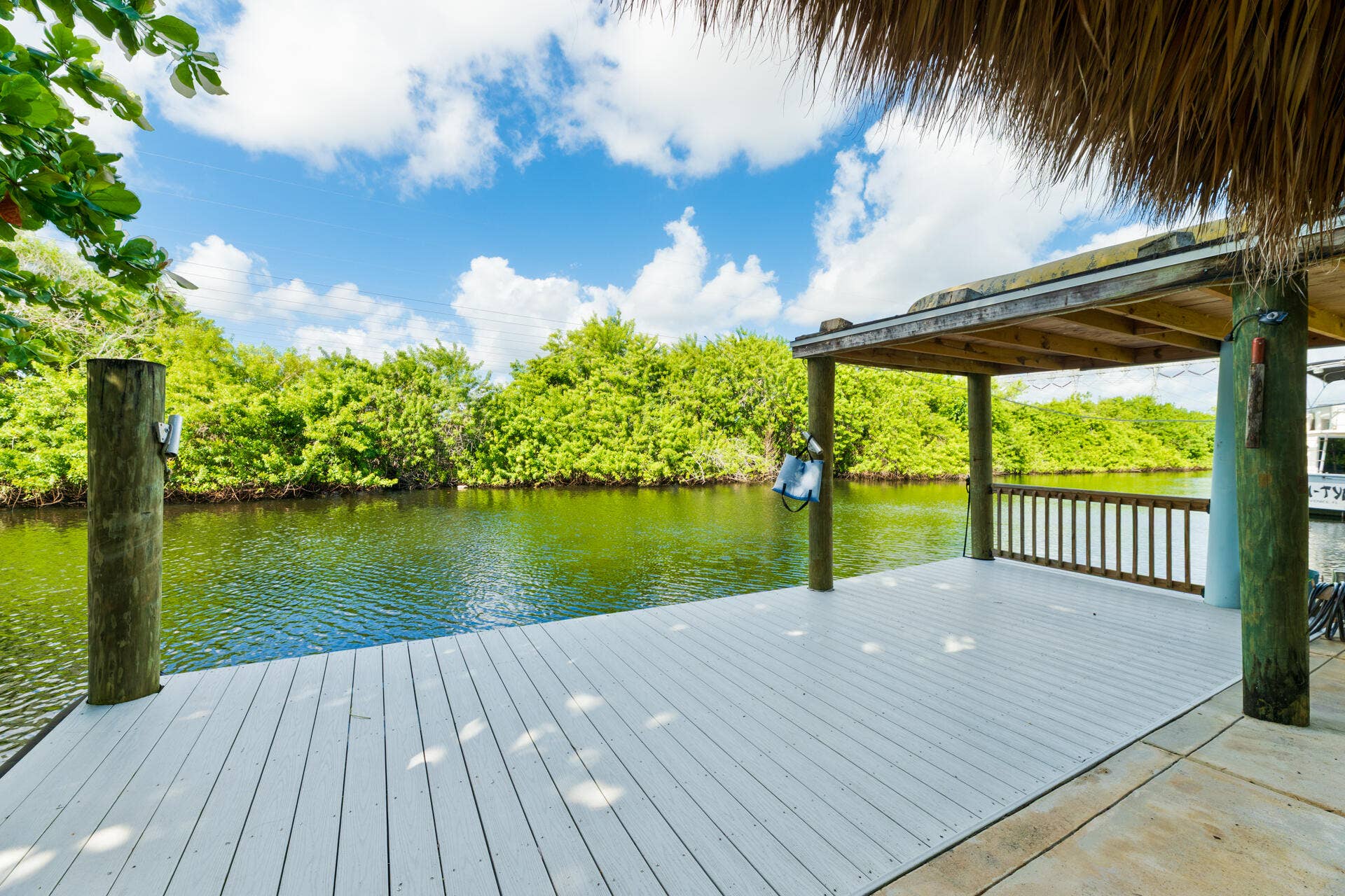 Waterfront dock featuring composite decking, a roof structure, timber pilings, and a wooden railing