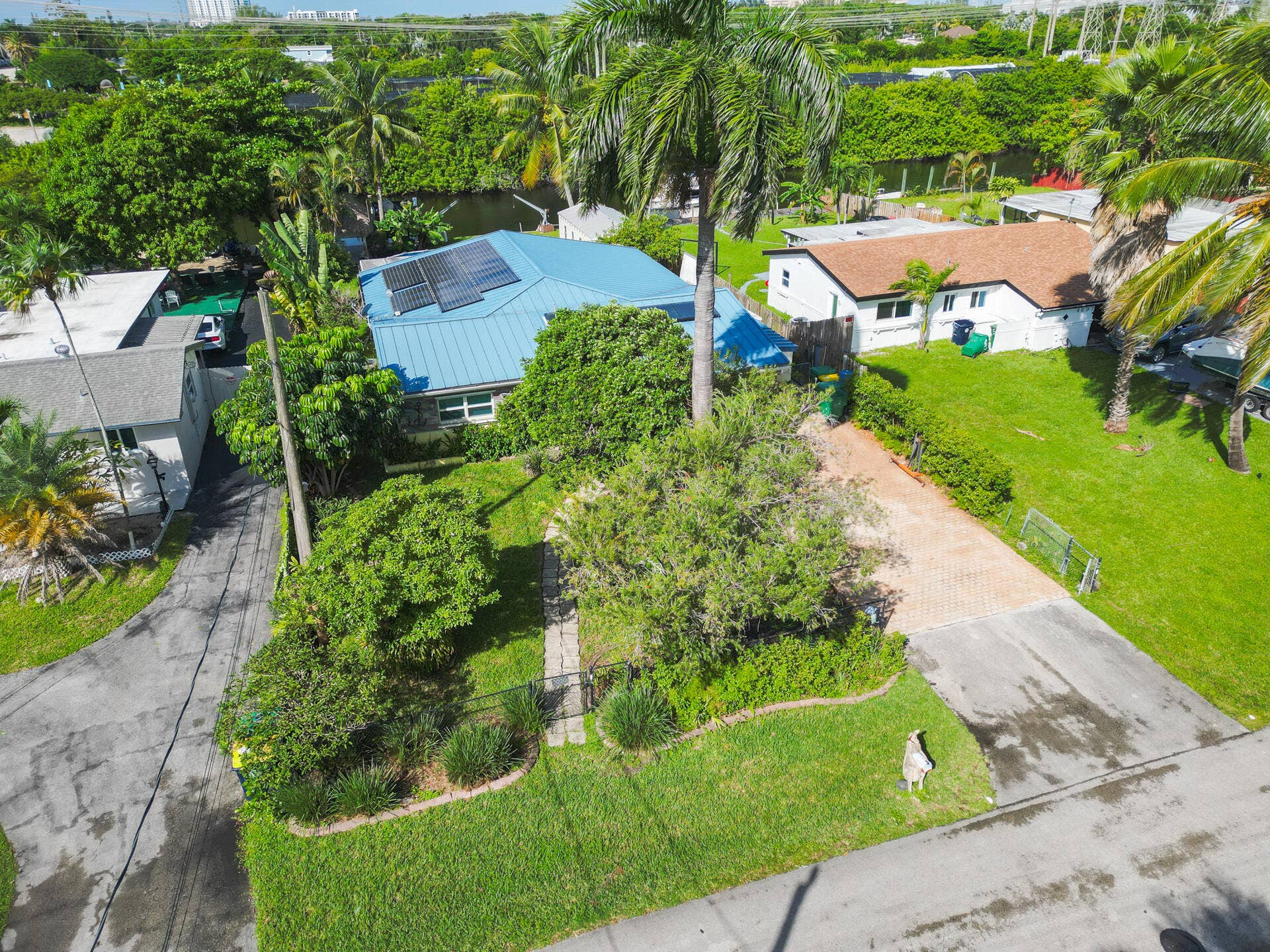Metal roofing system featuring 28 mounted solar panels, paved driveway, stone-accented exterior, and manicured landscaping with mature palm trees