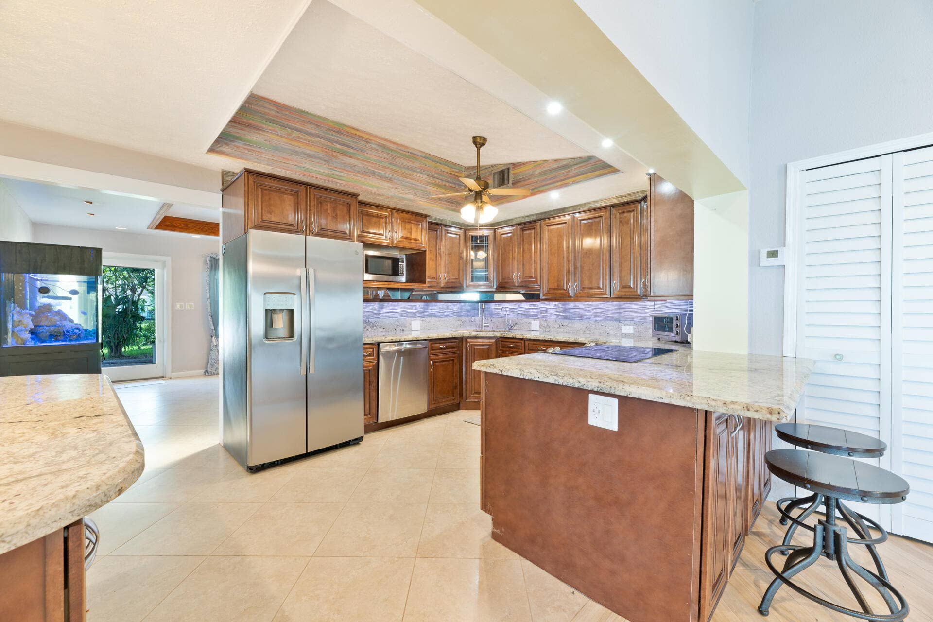Kitchen featuring stained wood cabinetry, stone countertops, stainless steel appliances, a recessed tray ceiling, and tile flooring