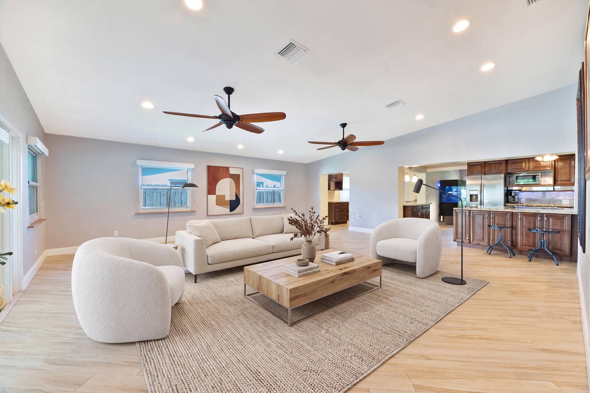 Open-concept interior featuring vaulted ceilings, recessed lighting, ceramic plank flooring, two dual-blade ceiling fans, and wood cabinetry with a breakfast bar