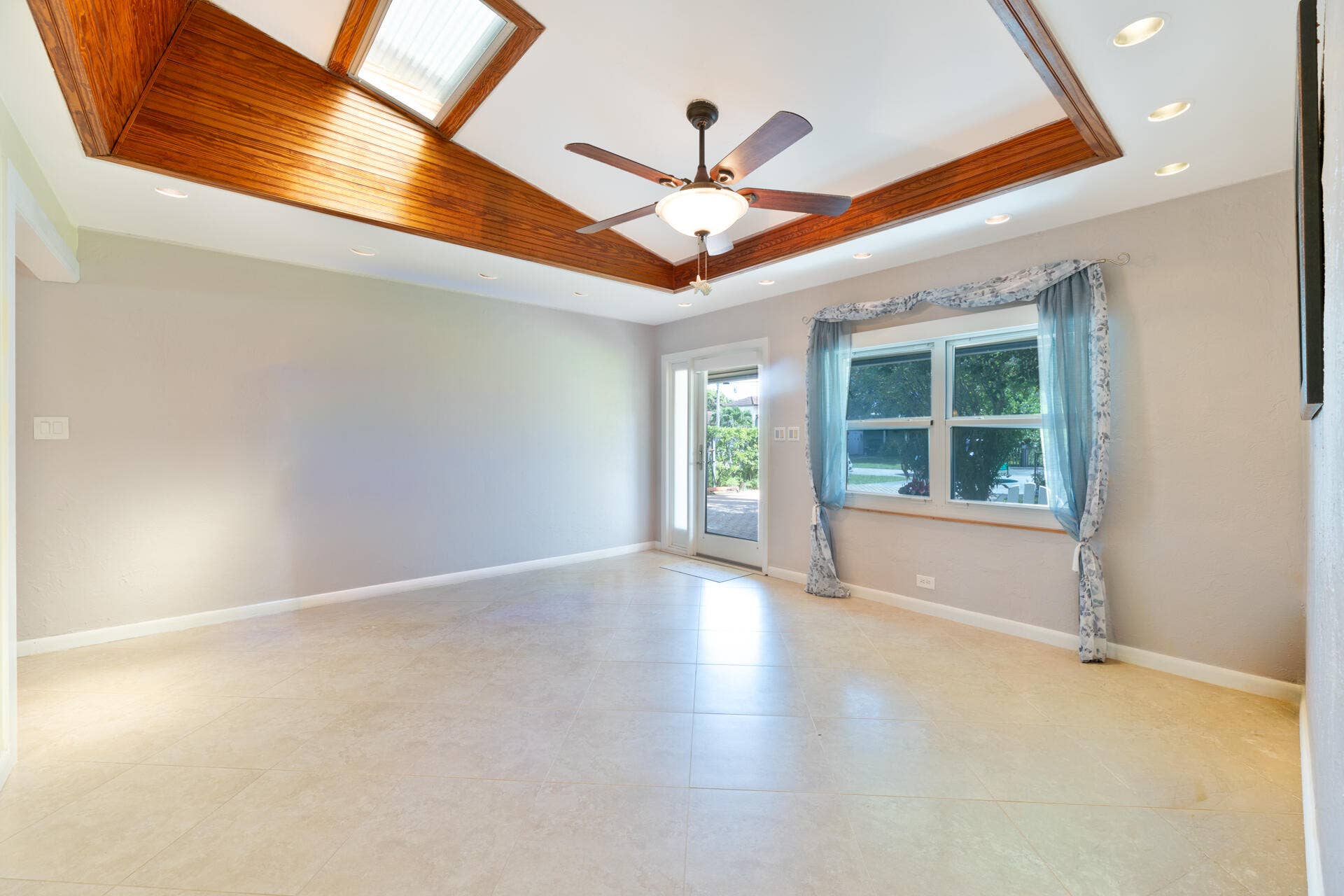 Vaulted ceiling with wood-trim detailing, recessed lighting, integrated skylight, ceiling fan, and tile flooring