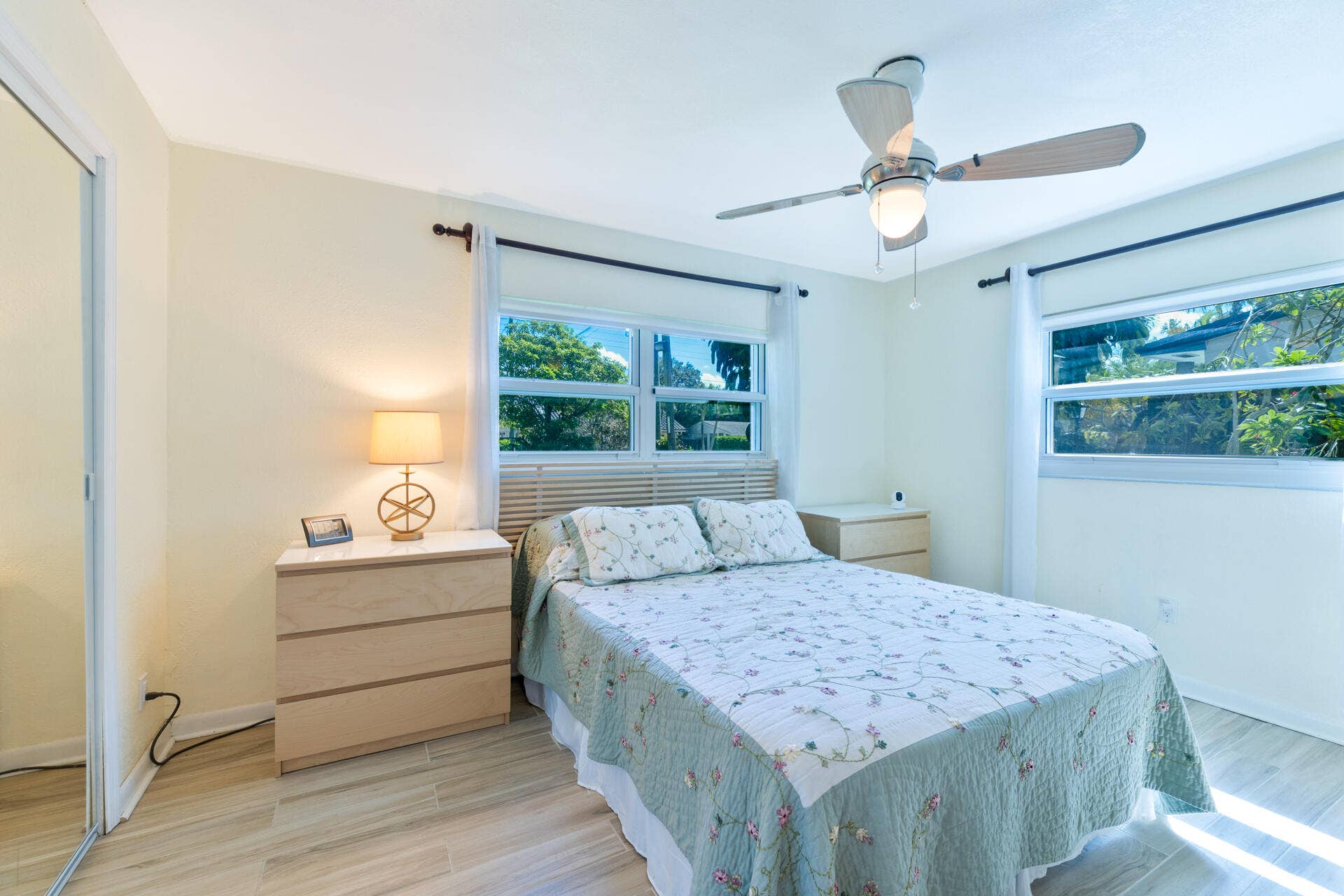 Neutral-toned room featuring ceramic plank flooring, a ceiling fan with integrated lighting, dual windows, and a mirrored sliding closet door
