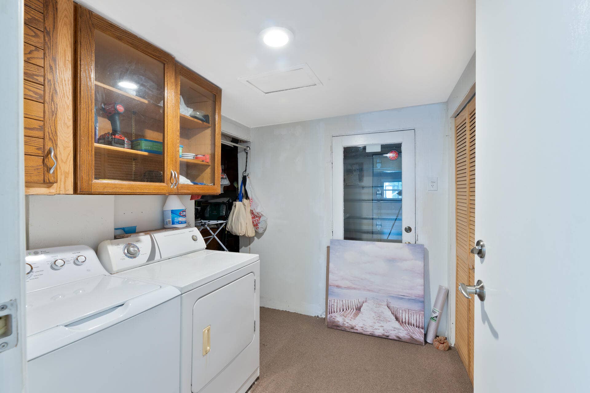 Utility area featuring wall-mounted wood cabinetry with glass-panel doors, louvered closet doors, and an exterior door with integrated window