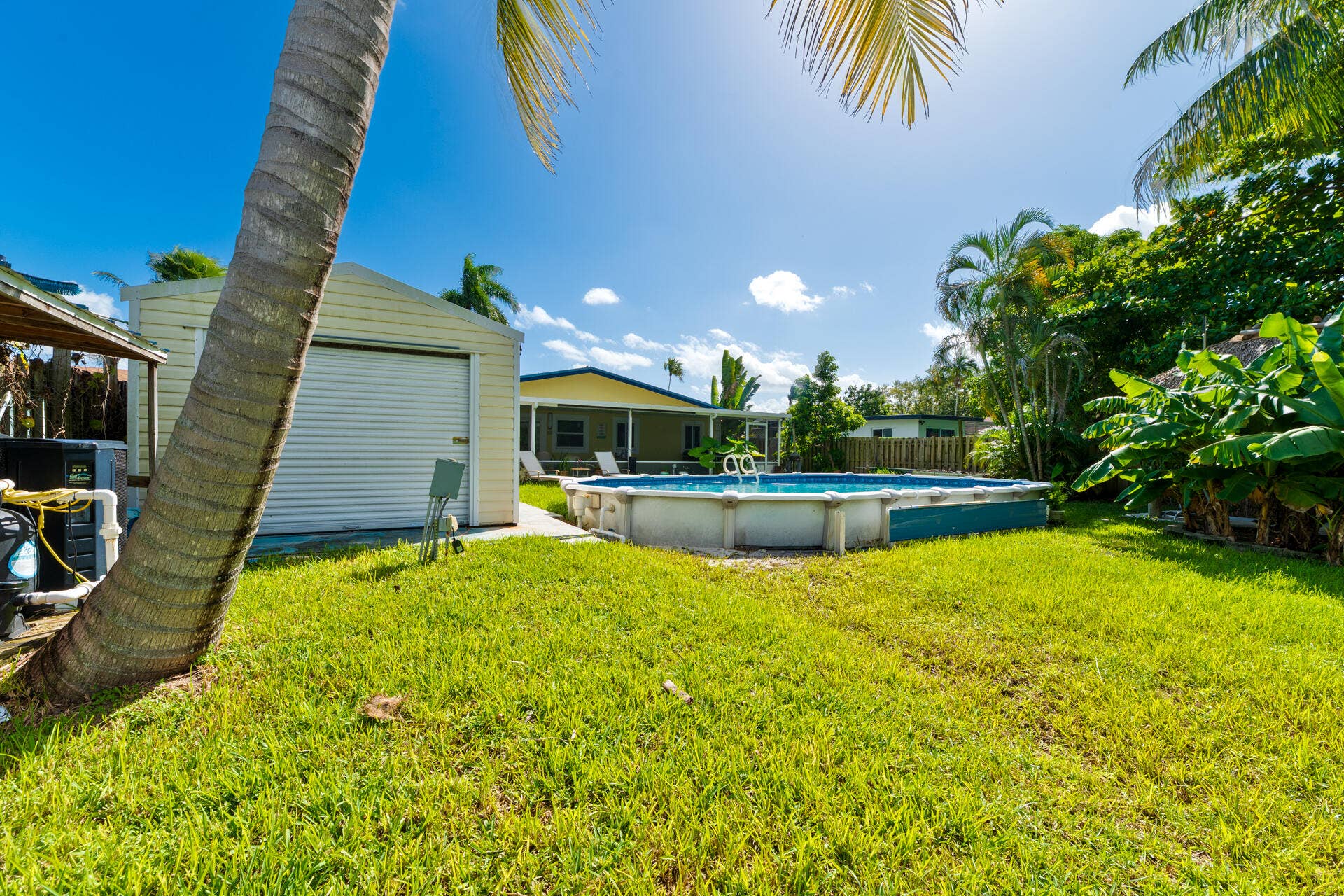 Backyard featuring a 33' round above-ground pool, detached storage structure with roll-up door, perimeter fencing, and mature palms