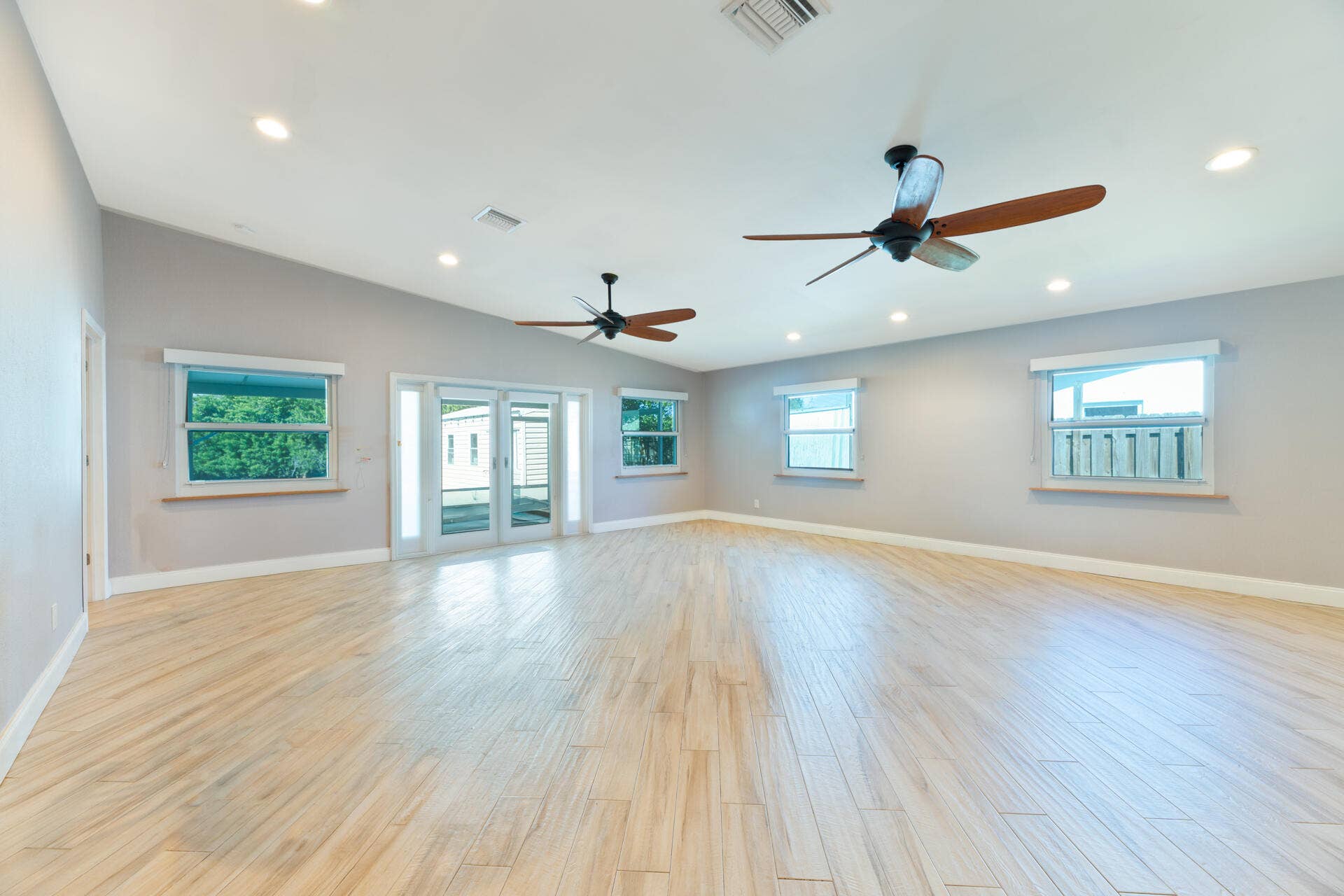 Spacious interior featuring ceramic plank flooring, vaulted ceilings, recessed lighting, dual ceiling fans, and glass-paned sliding doors