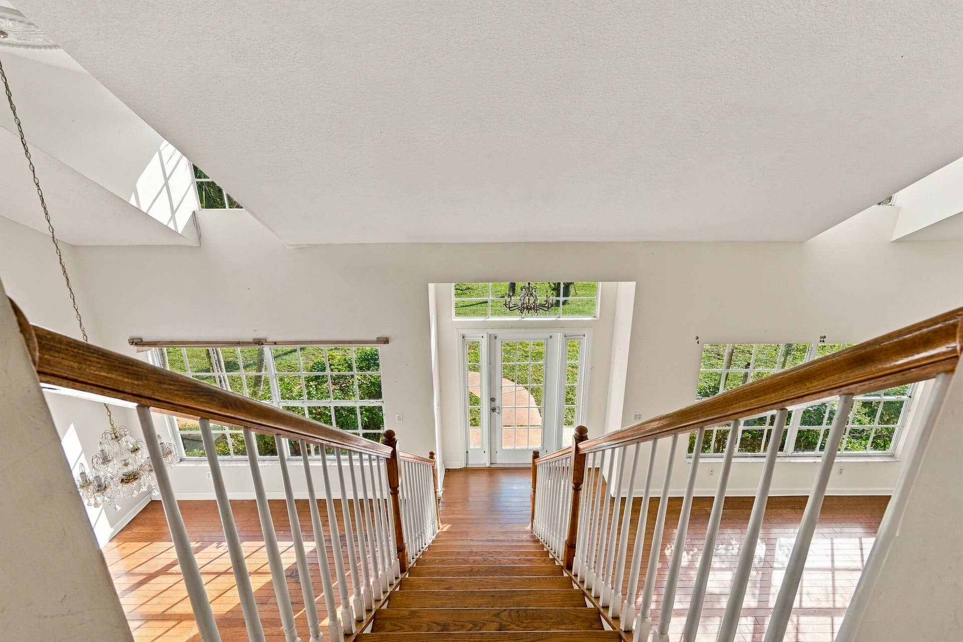High-ceiling foyer featuring wood-finish flooring, a grand staircase with white balusters and a wood handrail, expansive multi-pane windows, and a glass-paneled entry door with a transom window