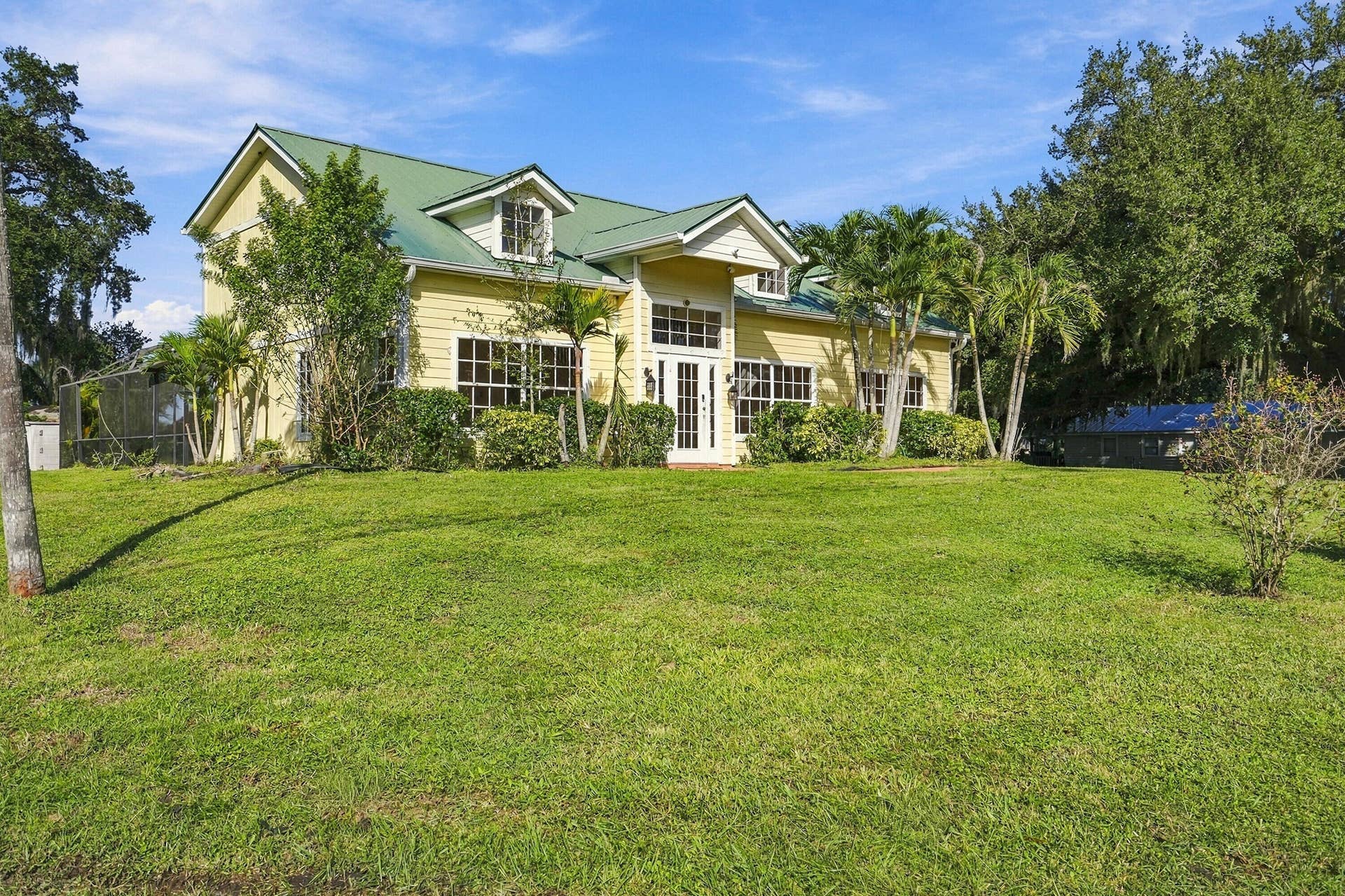 Two-story home with a green metal roof, light yellow horizontal siding, multi-pane windows, and a screened-in enclosure