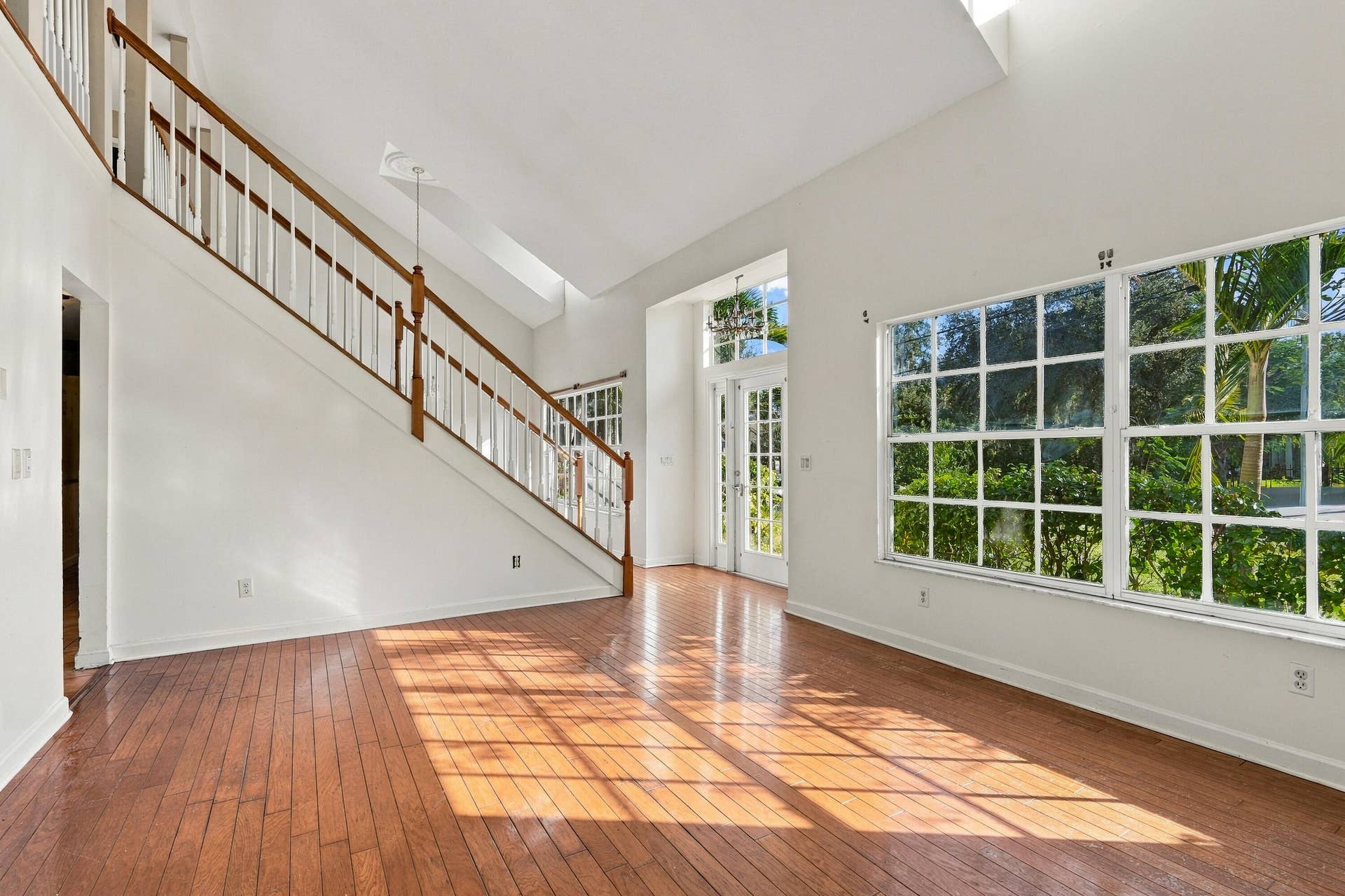 Vaulted ceilings, wood-finish flooring, staircase with wood railings, multiple pane windows, and a glass-paneled entry door