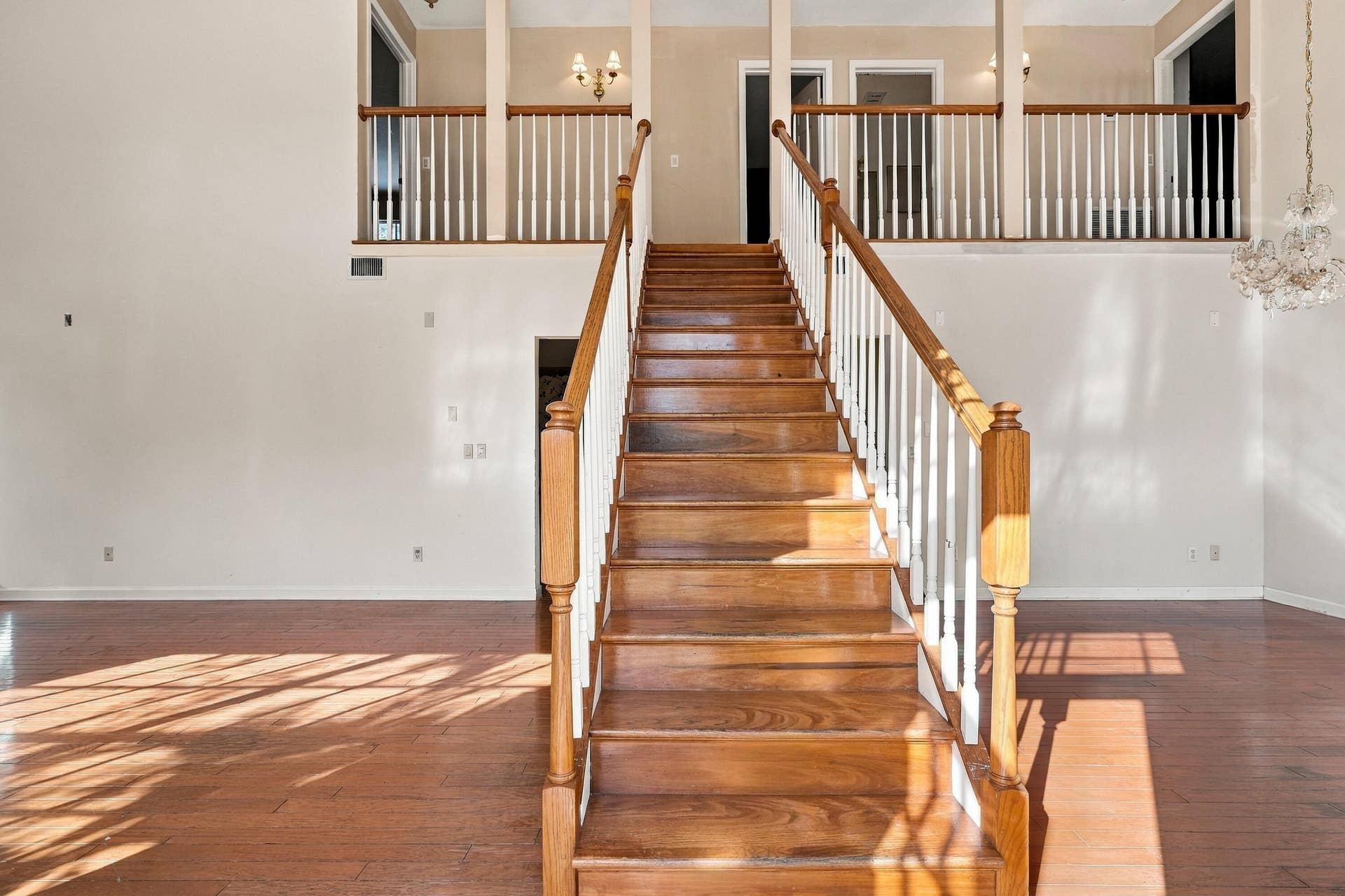 Open foyer featuring a wood-finish staircase with a custom wooden handrail, white vertical balusters, wood-finish flooring, and a decorative glass chandelier